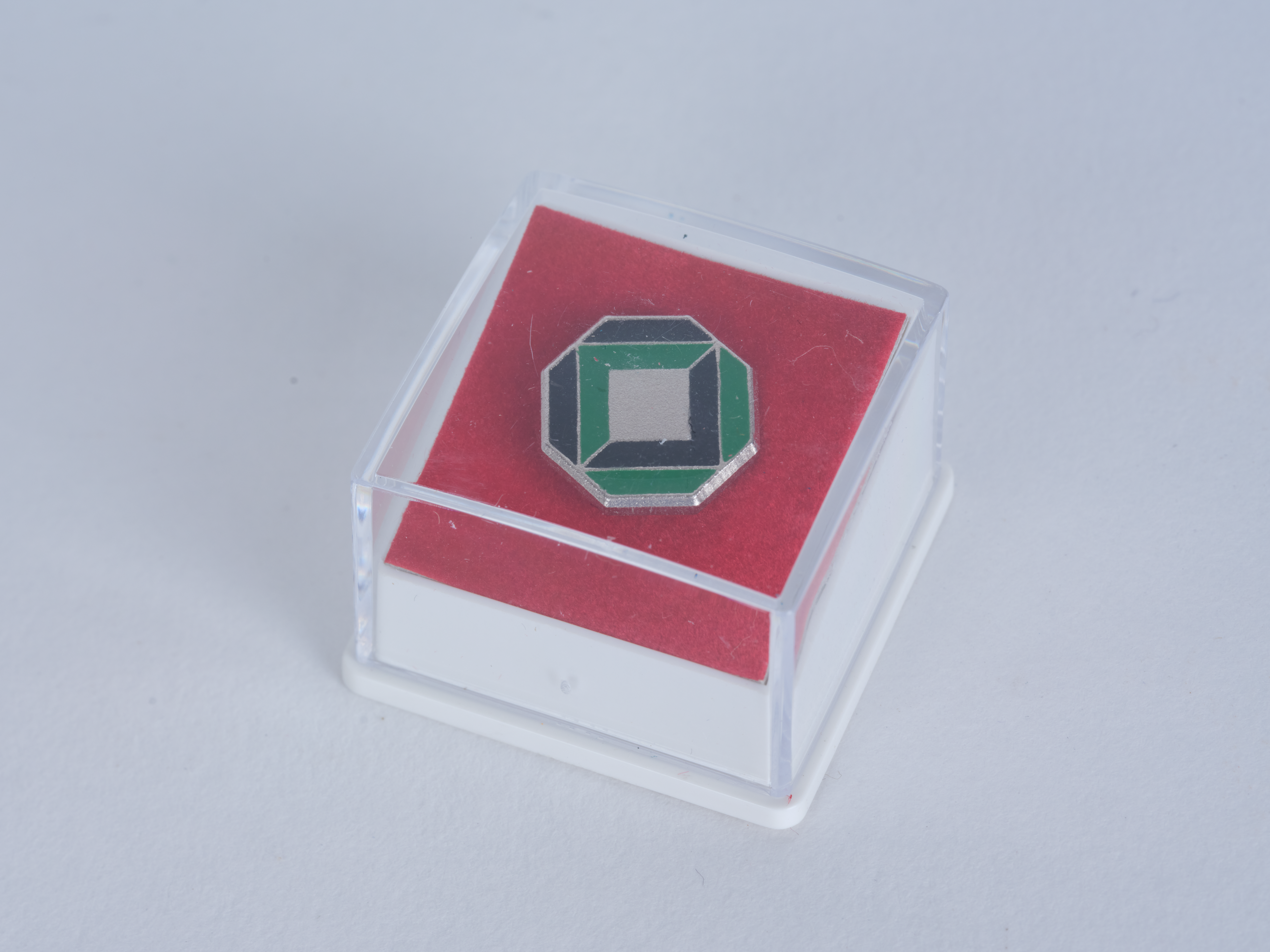 Pin with the logo of Karlsruhe University, approx. 1990, 12.5 mm, metal and synthetic resin. KIT Archives 28502/68. Photograph: Amadeus Bramsiepe and Jonas Zilius.